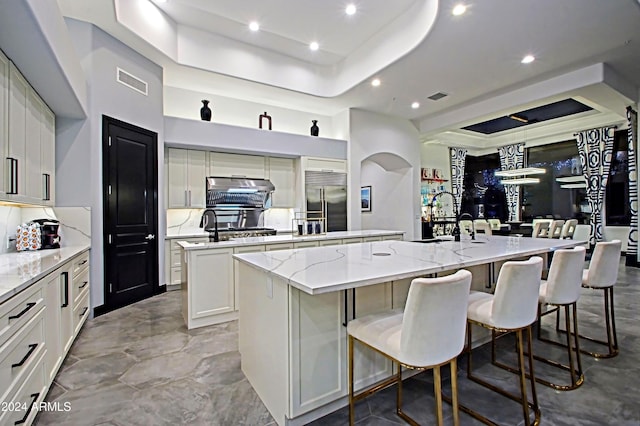 kitchen with light stone countertops, a large island with sink, built in refrigerator, and sink