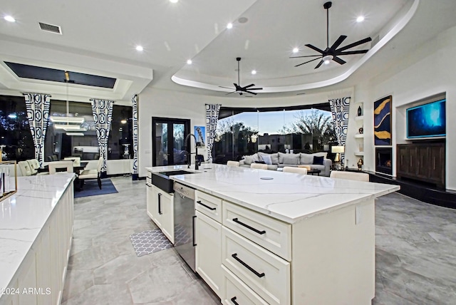 kitchen featuring light stone countertops, a large island with sink, a raised ceiling, and stainless steel dishwasher