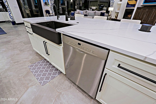 kitchen featuring light stone countertops, white cabinetry, stainless steel dishwasher, and sink