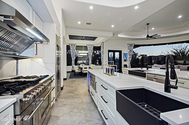 kitchen featuring white cabinets, high end stove, a raised ceiling, and light stone counters