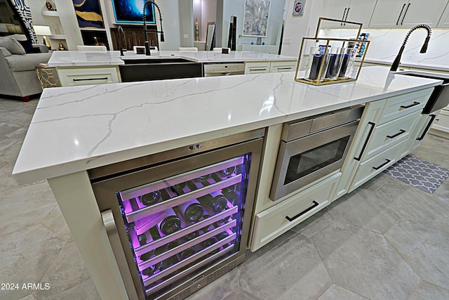 kitchen with a kitchen island, light stone counters, sink, and wine cooler