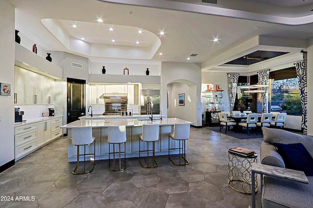 kitchen with tasteful backsplash, a tray ceiling, stainless steel built in fridge, white cabinetry, and a large island