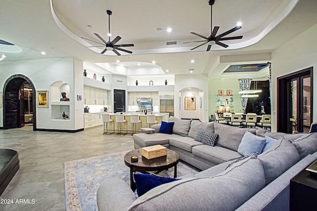 living room with a tray ceiling, ceiling fan, and built in features