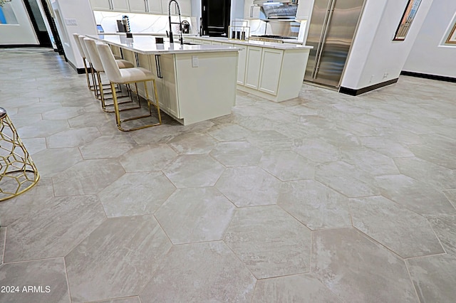 kitchen featuring a breakfast bar area, a kitchen island with sink, sink, and white cabinets