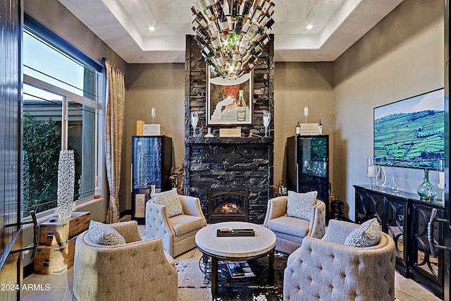 living room featuring a raised ceiling, a stone fireplace, and light tile patterned flooring