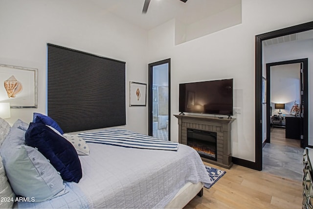 bedroom featuring a brick fireplace, ceiling fan, ensuite bathroom, and light hardwood / wood-style flooring