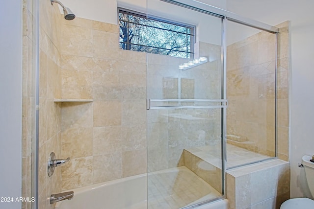 bathroom featuring toilet and bath / shower combo with glass door