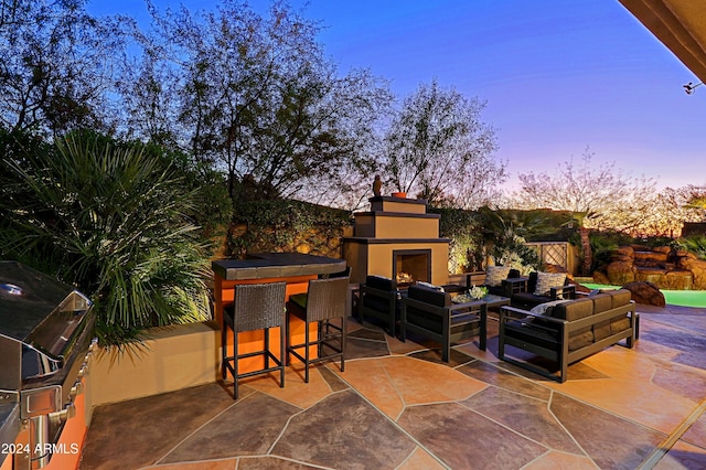 patio terrace at dusk featuring an outdoor living space with a fireplace, area for grilling, and exterior bar