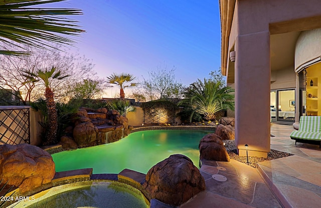 pool at dusk with an in ground hot tub and a patio area