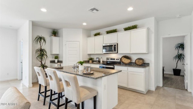 38100 W Bello Ln, Maricopa, AZ 85138 - kitchen with appliances with stainless steel finishes, a kitchen island with sink, dark stone countertops, white cabinetry, and a breakfast bar area