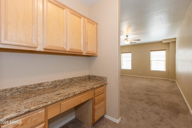 interior space featuring baseboards, a ceiling fan, built in desk, and light colored carpet