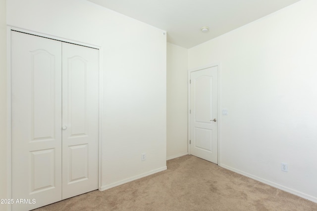 unfurnished bedroom with baseboards, light colored carpet, and a closet