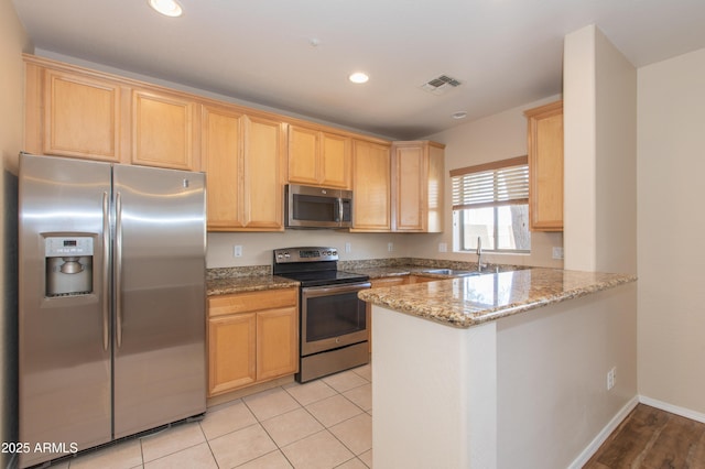 kitchen with visible vents, a peninsula, light stone countertops, a sink, and appliances with stainless steel finishes