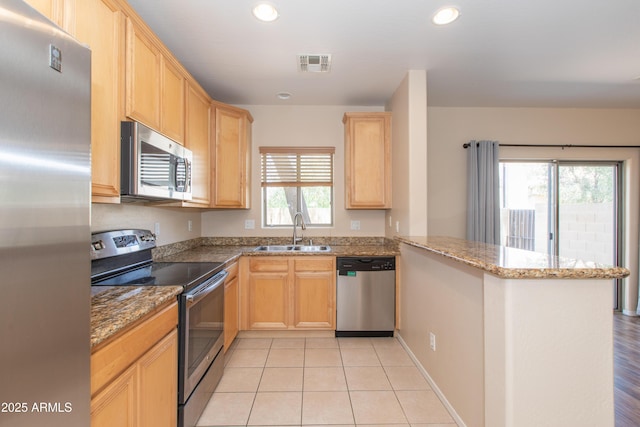 kitchen featuring visible vents, a sink, a peninsula, light brown cabinets, and stainless steel appliances