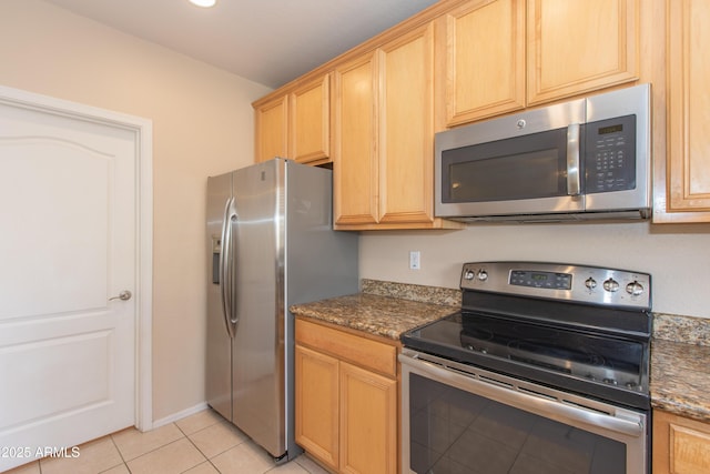 kitchen with light tile patterned floors, appliances with stainless steel finishes, light brown cabinetry, and dark stone counters
