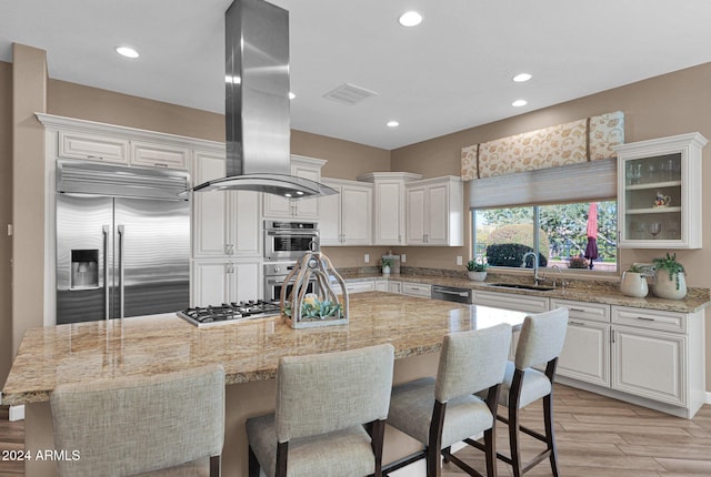 kitchen featuring light stone countertops, appliances with stainless steel finishes, a kitchen island, white cabinetry, and island exhaust hood