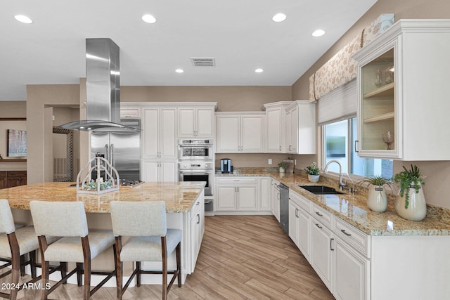 kitchen featuring island range hood, stainless steel appliances, sink, white cabinets, and light hardwood / wood-style floors