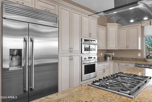 kitchen featuring light stone countertops, exhaust hood, and appliances with stainless steel finishes