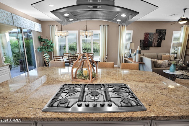 kitchen with light stone countertops, ceiling fan with notable chandelier, plenty of natural light, and stainless steel gas stovetop