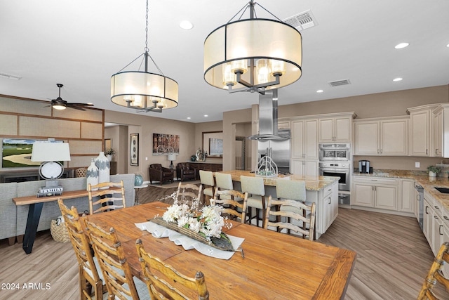 dining room with ceiling fan with notable chandelier and light hardwood / wood-style floors