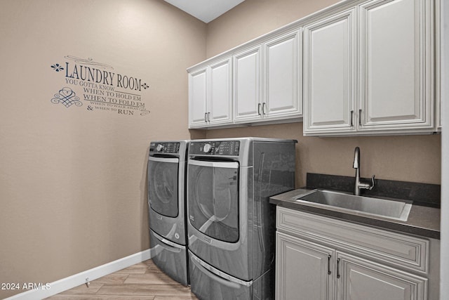 laundry room with cabinets, sink, washer and dryer, and light hardwood / wood-style flooring