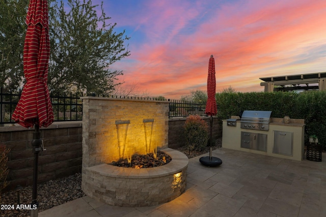 patio terrace at dusk featuring area for grilling, a grill, and an outdoor fire pit