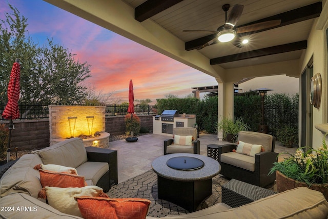 patio terrace at dusk with an outdoor living space with a fire pit, area for grilling, ceiling fan, and exterior kitchen