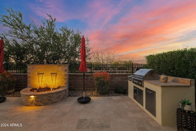 patio terrace at dusk featuring a grill, exterior kitchen, and an outdoor fire pit