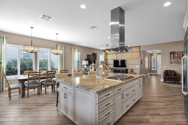 kitchen with white cabinetry, island exhaust hood, an island with sink, wood-type flooring, and stainless steel gas stovetop