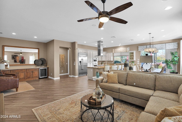 living room with wine cooler, ceiling fan with notable chandelier, and hardwood / wood-style flooring