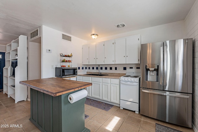 kitchen featuring butcher block countertops, white cabinetry, sink, light tile patterned floors, and stainless steel appliances