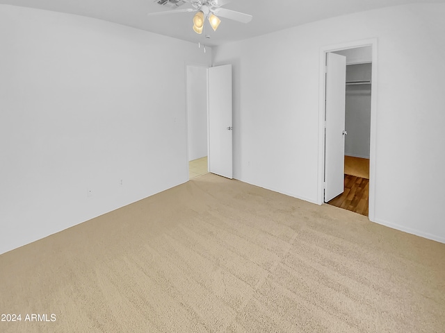 unfurnished bedroom with light carpet, a closet, ceiling fan, and a walk in closet