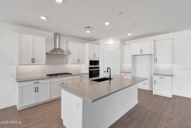 kitchen with white cabinets, black oven, sink, and wall chimney exhaust hood