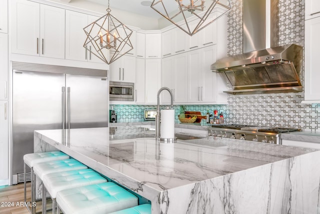 kitchen featuring pendant lighting, a breakfast bar, light stone counters, white cabinets, and wall chimney exhaust hood