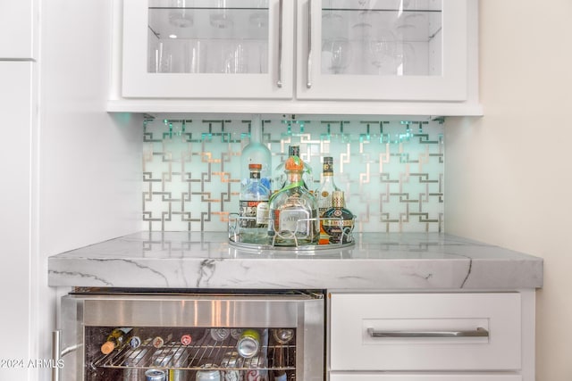 bar with white cabinetry, backsplash, light stone counters, and beverage cooler