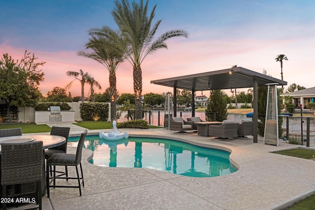 pool at dusk with area for grilling, outdoor lounge area, and a patio