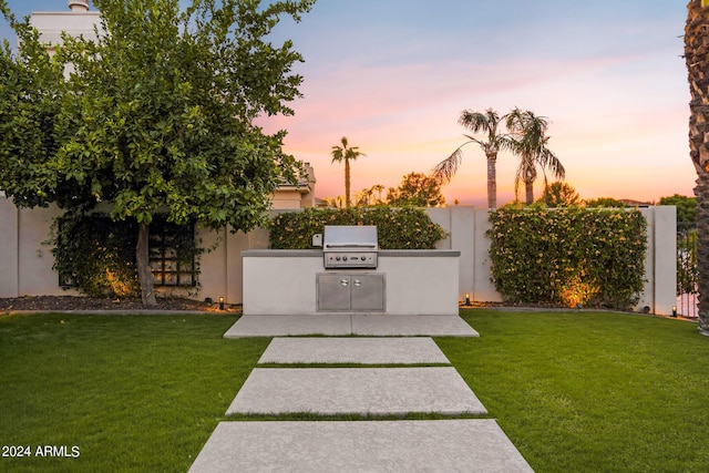 yard at dusk featuring a patio and an outdoor kitchen