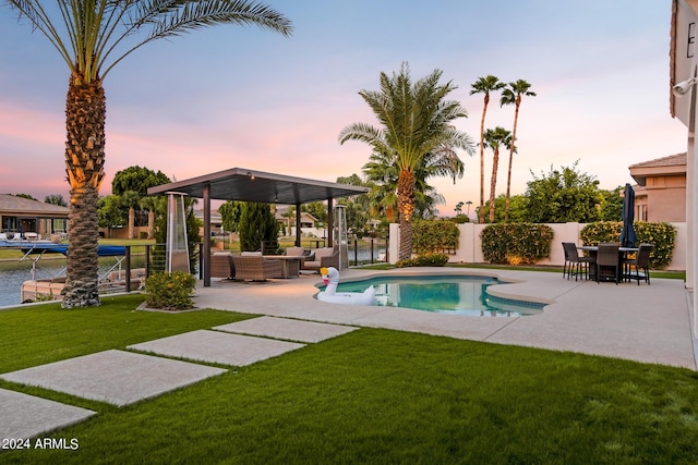 pool at dusk with outdoor lounge area, a lawn, and a patio area