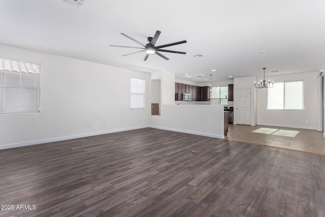 unfurnished living room featuring ceiling fan with notable chandelier and dark wood-type flooring