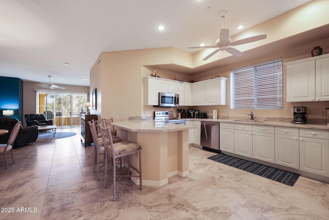 kitchen with sink, a breakfast bar, stainless steel appliances, white cabinets, and kitchen peninsula