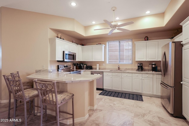 kitchen with sink, a breakfast bar area, kitchen peninsula, stainless steel appliances, and white cabinets