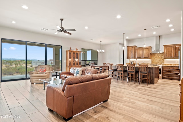 living room featuring ceiling fan with notable chandelier, light hardwood / wood-style flooring, and sink