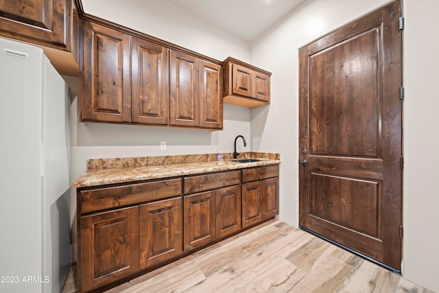 kitchen featuring white refrigerator, light stone countertops, light hardwood / wood-style floors, and sink