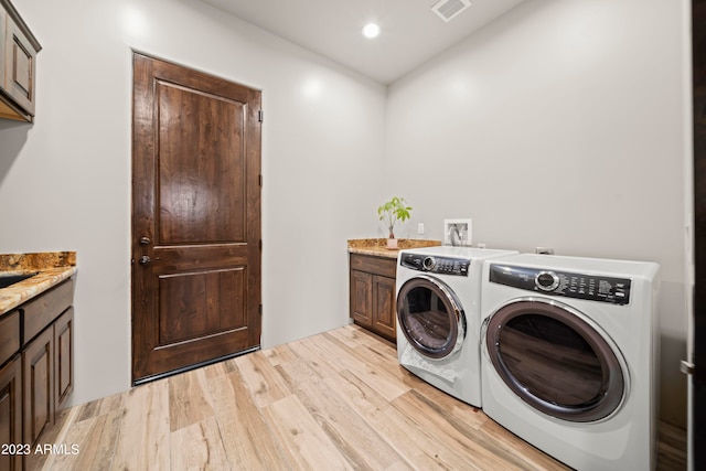 laundry room featuring washing machine and clothes dryer, cabinets, and light hardwood / wood-style flooring