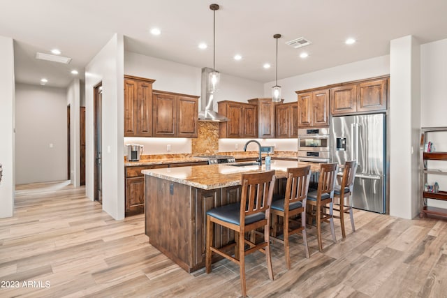 kitchen with an island with sink, light wood-type flooring, light stone countertops, stainless steel appliances, and sink