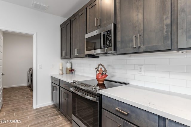 kitchen with appliances with stainless steel finishes, light wood-type flooring, tasteful backsplash, dark brown cabinetry, and washing machine and dryer