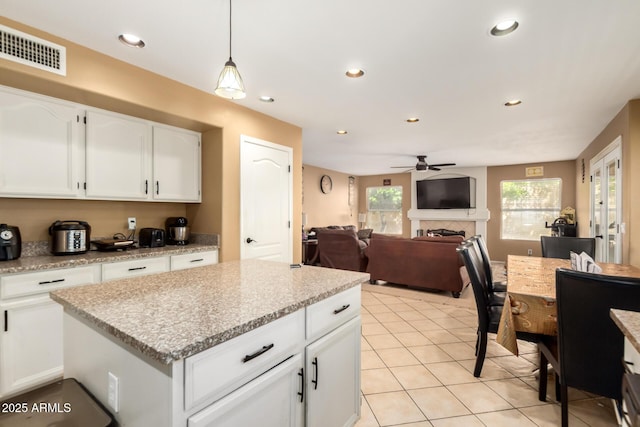 kitchen with a fireplace, light tile patterned floors, visible vents, open floor plan, and white cabinetry