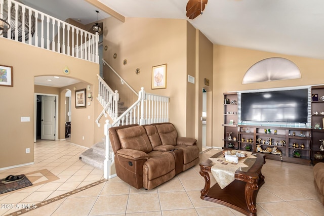 living area with arched walkways, high vaulted ceiling, tile patterned flooring, baseboards, and stairway