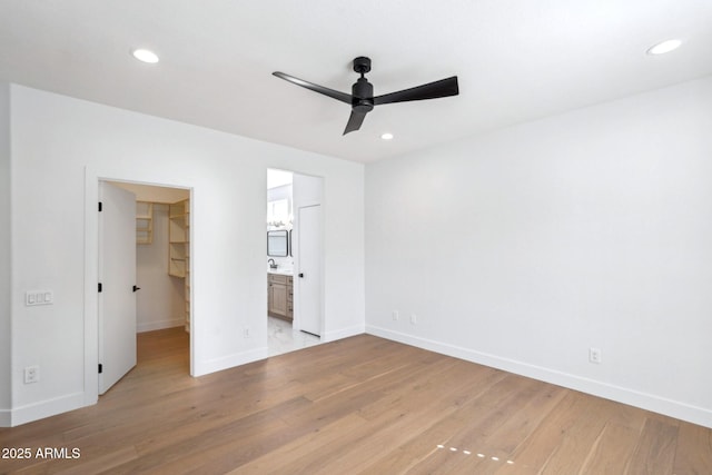 unfurnished bedroom featuring ensuite bathroom, a spacious closet, light wood-type flooring, a closet, and ceiling fan