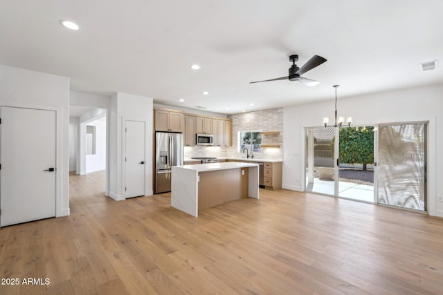 kitchen with appliances with stainless steel finishes, a center island, pendant lighting, and light wood-type flooring